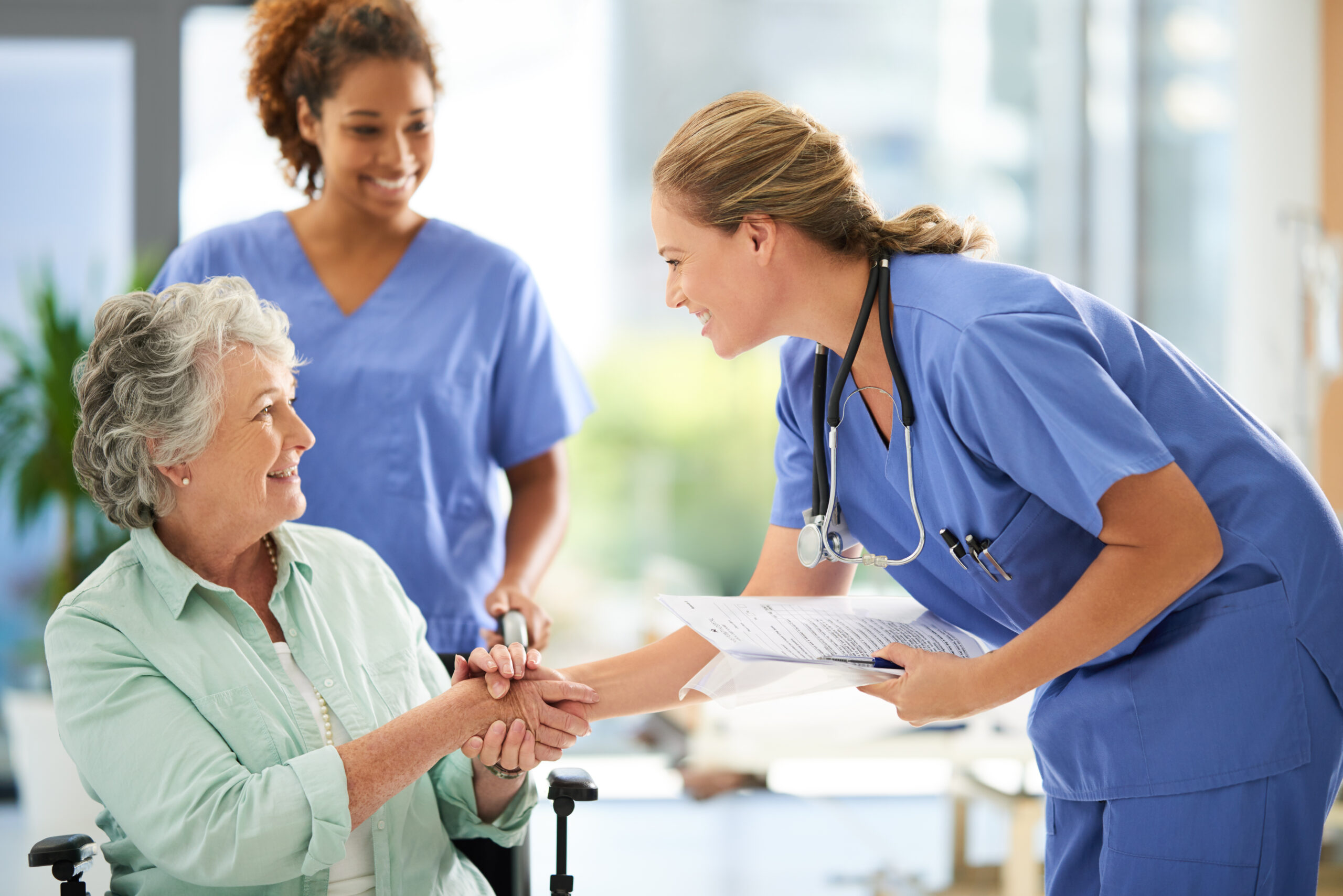 shot of an attractive female nurse holding medical records while shaking hands with her wheelchair bound senior patient in the hospital